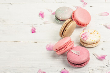 Macarons with peony flower petals on a white wooden background. Sweet dessert, pastel colors