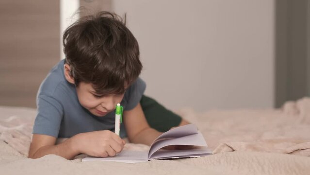asian boy draws or writes in the bed. elementary school student draw or hand writing in diary by pencil. cozy home atmosphere