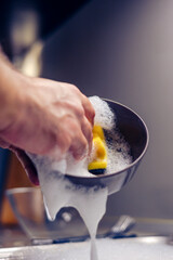 A brown glass plate in the hands of a man who is washing dishes in the kitchen.