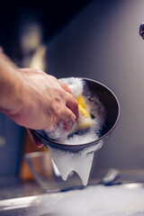 A brown glass plate in the hands of a man who is washing dishes in the kitchen.