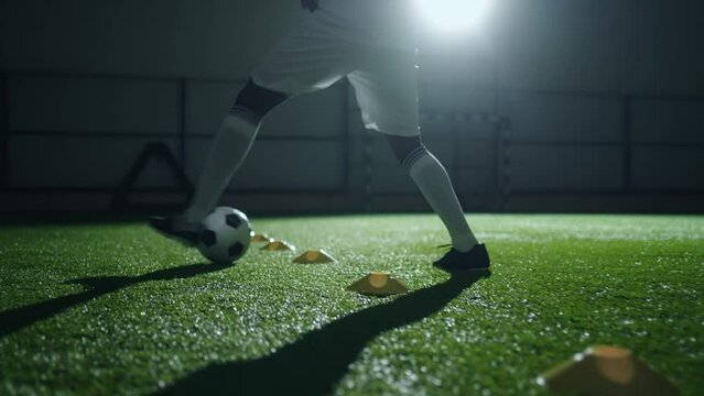 junior football player training alone in gym, dribbling and doing feint with ball