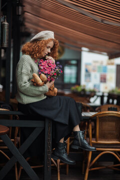 Woman portrait in a beret sweater holding a bouquet of flowers of the restaurant background 