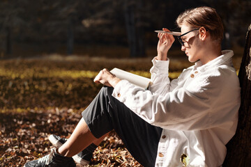 Woman sitting on ground in park with  diary on her lap and thinking about notes in notebook.
