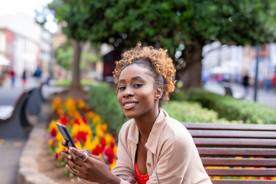cool young african american woman sitting outside on street with cellphone