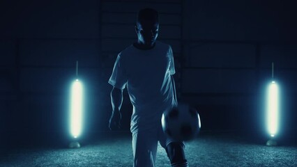 young african american man training football tricks, kicking ball by knee in dark stadium, portrait - Powered by Adobe