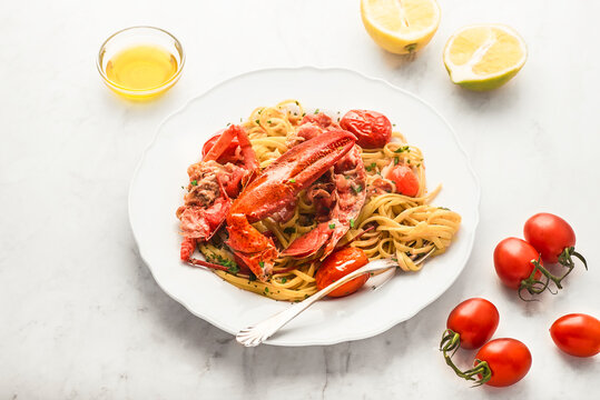Lobster linguine  pasta   with ingredients for cooking. Lemon, tomatoes, olive oil, parsley on the white marble  table. Delicatessen, rare seafood pasta recipe. Sardinia, Sicilian, Neapolitan cuisine.