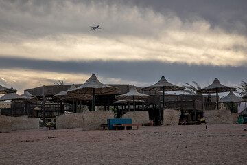 Old abandoned beach. Sun umbrellas. Colorful evening. The plane takes off in the sky. Sand underfoot.