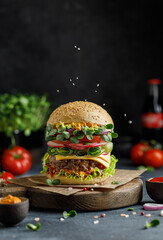 Burger with beef, cheese, green salad, tomato and onion on wooden board. American food concept. Fast food meal.
