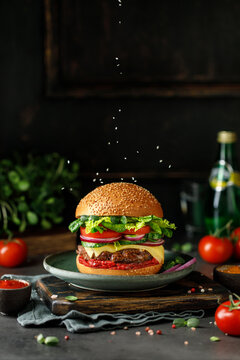 Burger with beef, cheese, green salad, tomato and onion on wooden board. American food concept. Fast food meal.
