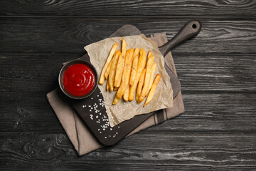 Delicious fresh french fries and tomato sauce on black wooden table, top view