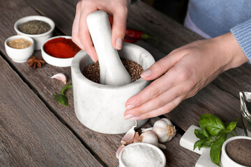 Woman grinding coriander at wooden table, closeup