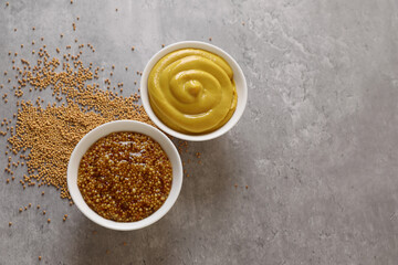 Bowls with mustard and seeds on grey table, flat lay. Space for text