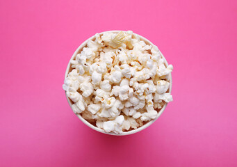 Paper bucket with delicious popcorn on pink background, top view