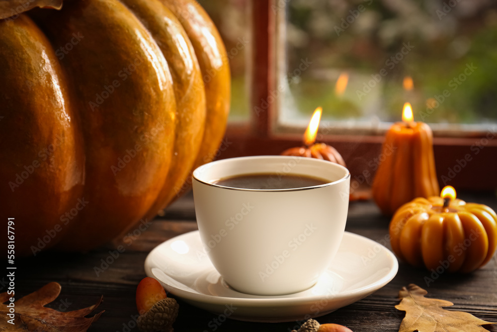 Sticker Cup of hot drink and pumpkin shaped candles on wooden table near window, closeup. Cozy autumn atmosphere