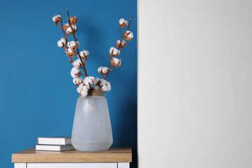 Cotton branches with fluffy flowers in vase and books on wooden table indoors. Space for text