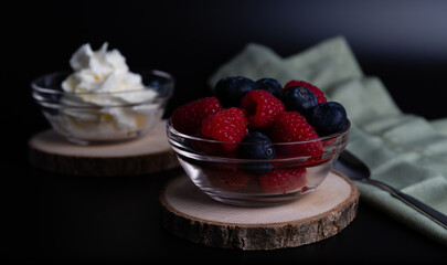 Blueberries and raspberries in a glass bowl and glass bowl with whipped cream. Macro shooting, all focus on berries.