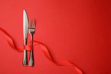 Cutlery set with ribbon on red background, flat lay and space for text. Romantic table setting