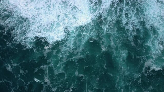Top aerial view of ocean waves splashing against rocks background. High quality 4k footage