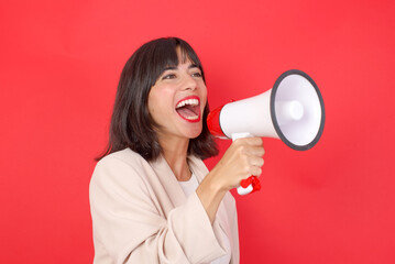 Young beautiful businesswoman with short black hair standing over red studio background holding a speaker and shouting. Promotion and sales concept. 