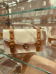 Fashionable white and brown color woman small handbag on the store glass shelf.