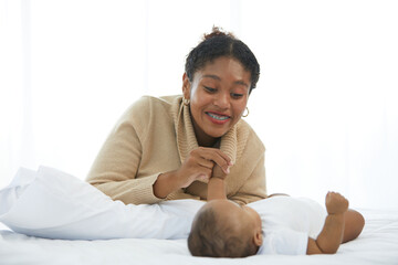 African young mother playing with her adorable baby on bed