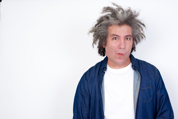 middle aged man with grey hair wearing denim jacket over white background expressing disgust, unwillingness, disregard having tensive look frowning face, looking indignant with something.