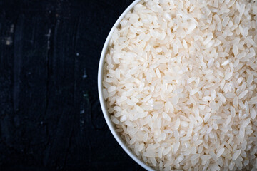 Bowl containing uncooked white rice on a black background. Top view. Close-up. Background and texture.