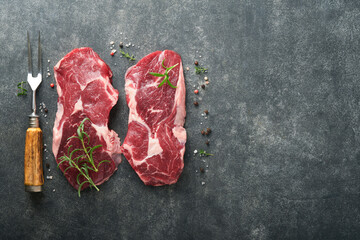 Raw beef steak. Marbled raw fresh Ribeye steak with rosemary, salt and pepper on cutting board on dark concrete background. Raw beef steak and spices for cooking.