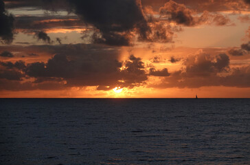 Obraz premium Dramatic sunset over ocean with tiny sailing boat