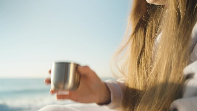 The girl at the sea finishes her Bagel and drinks tea from a thermos. Close-up.