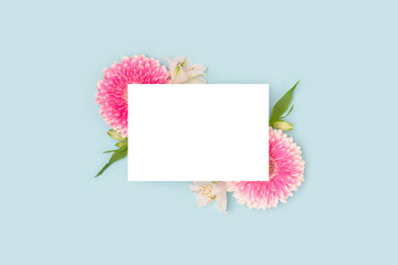 Clean paper mock up. Frame made of green leaves, alstroemeria and pink gerbera flowers on a blue background.