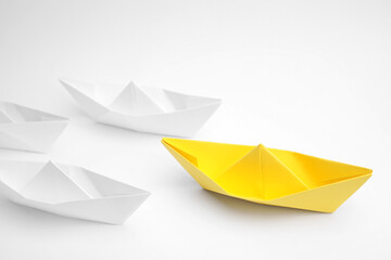 Group of paper boats following yellow one on white background, above view. Leadership concept