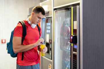 Athlete in gym consuming drink from food vending machine - obrazy, fototapety, plakaty