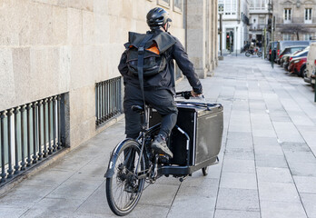 Courier man riding a cargo bike along the city on his way to deliver a package - obrazy, fototapety, plakaty