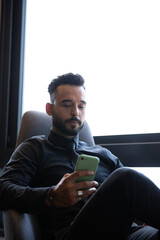 handsome young man wearing beard sitting looking at his phone, man answering message on cell phone