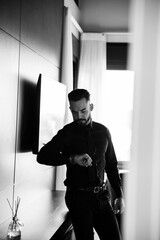 handsome man standing in his bedroom wearing black business suit looking at his watch, black and white photography