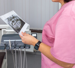 Dentist woman in pink uniform looking at roentgen of human jaw.