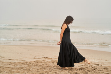 an unrecognizable woman in a black dress on the shore of the ocean pensive and melancholic