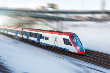 High-speed suburban electric train rushes along the railway tracks on snow winter day, motion blur effect.