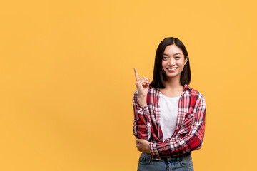 Inspiration, solution concept. Happy young asian lady raising finger up and smiling at camera, yellow background