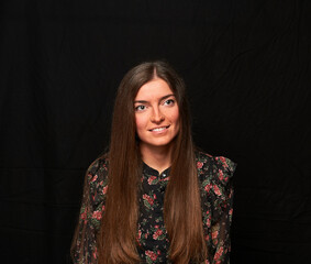 smiling girl in a black shirt with a flower print and long hair poses on a black cloth in the background