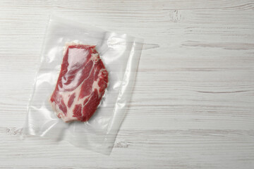 Raw beef in vacuum pack on white wooden table, top view. Space for text
