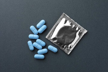 Fototapeta na wymiar Pills and condom on dark gray background, flat lay. Potency problem