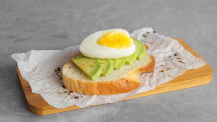 Delicious sandwich with boiled egg and pieces of avocado on gray table