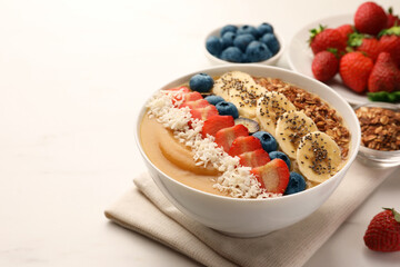 Delicious smoothie bowl with fresh berries, banana, coconut flakes and granola on white table. Space for text