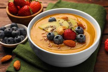 Delicious smoothie bowl with fresh berries, kiwi and nuts on wooden table, closeup