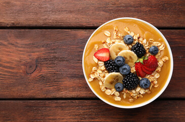 Delicious smoothie bowl with fresh berries, banana and oatmeal on wooden table, top view. Space for text