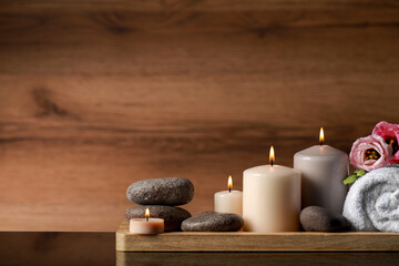 Beautiful composition with spa stones, flowers and burning candles on mirror table against wooden background. Space for text