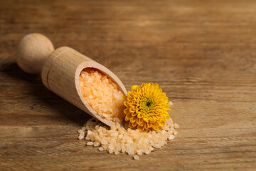 Scoop with orange sea salt and beautiful flower on wooden table. Space for text