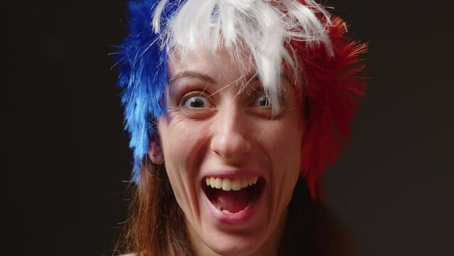 A woman with a mohawk on her head in the color of the French flag supports her sports team. Football fan at the stadium rejoices at the victory of his team